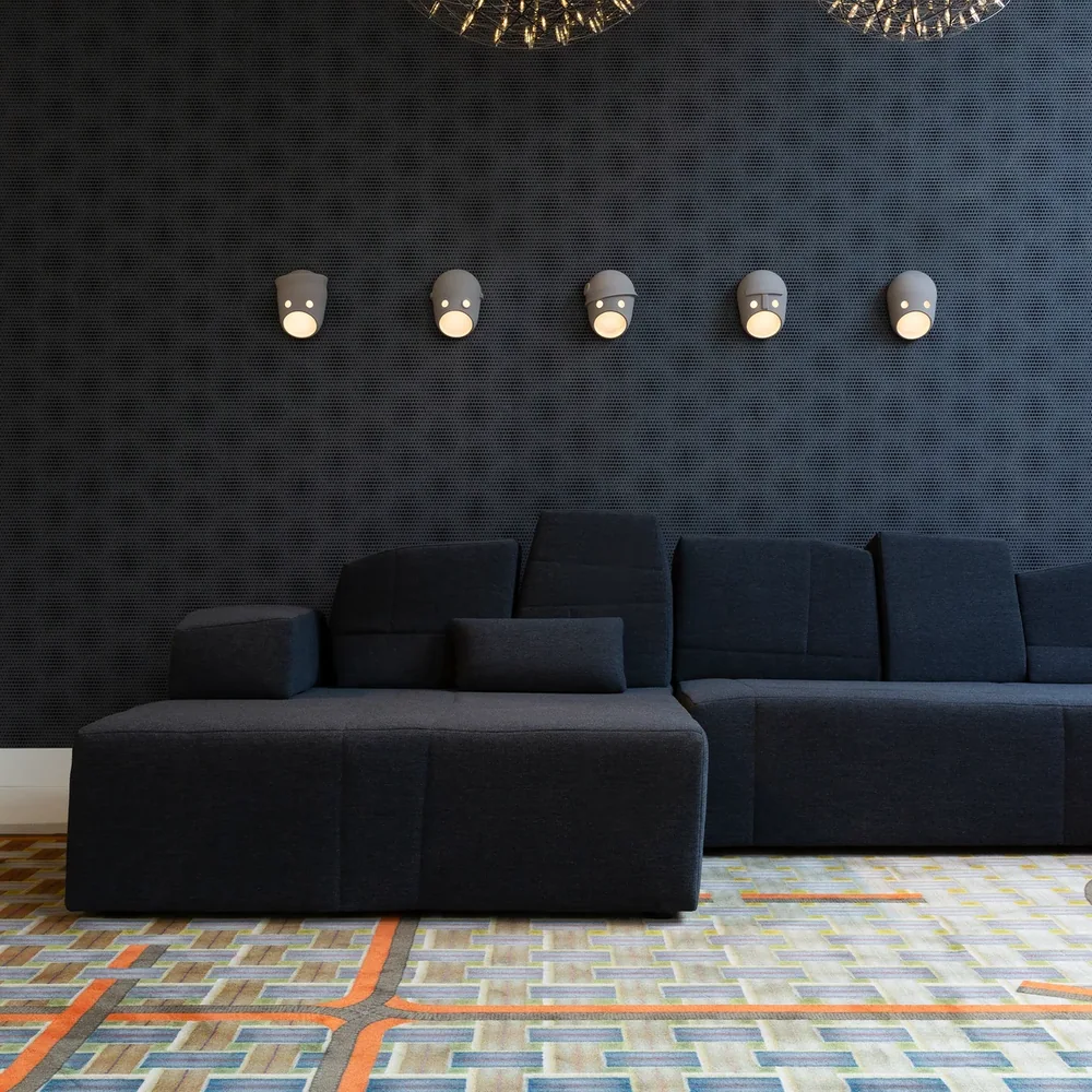 Moooi: Dunkle Wohnrauminszenierung mit zwei großen kugeligen Lichtobjekten, mehreren Gesichts-Wandleuchten und Sofa.
