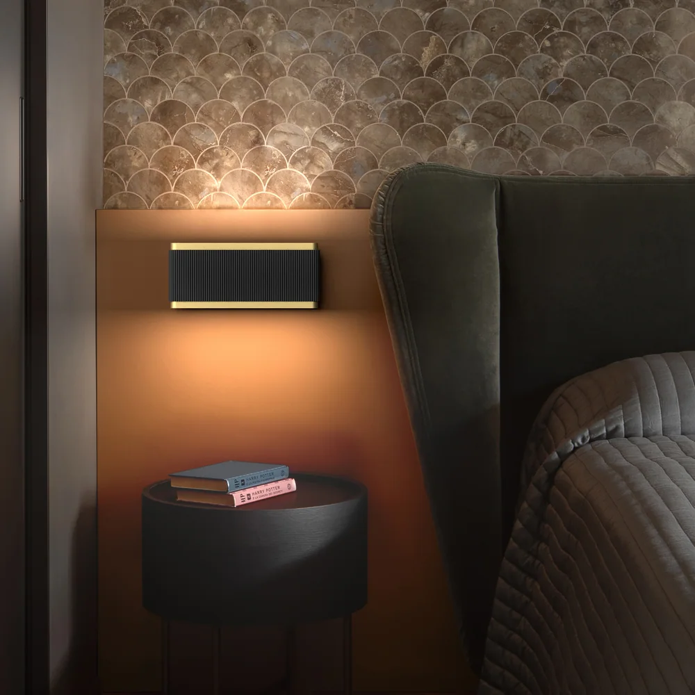 Rotaliana: Kompakte Leuchte in einer dunklen Halterung neben einem Bett, mit warmem Licht an der Wand.